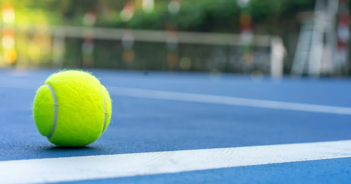 Balle de tennis posée sur un court en dur bleu, près d'une ligne