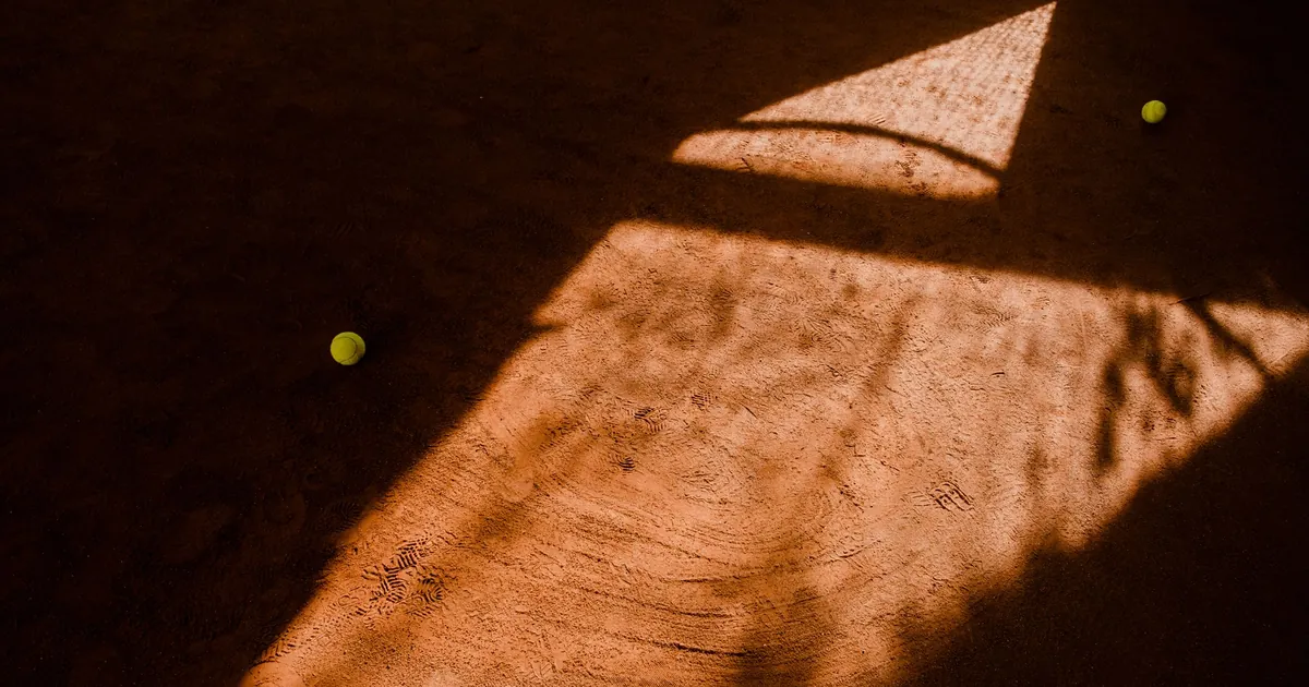Court de terre battue en plein soleil, balles entre la lumière et l'ombre