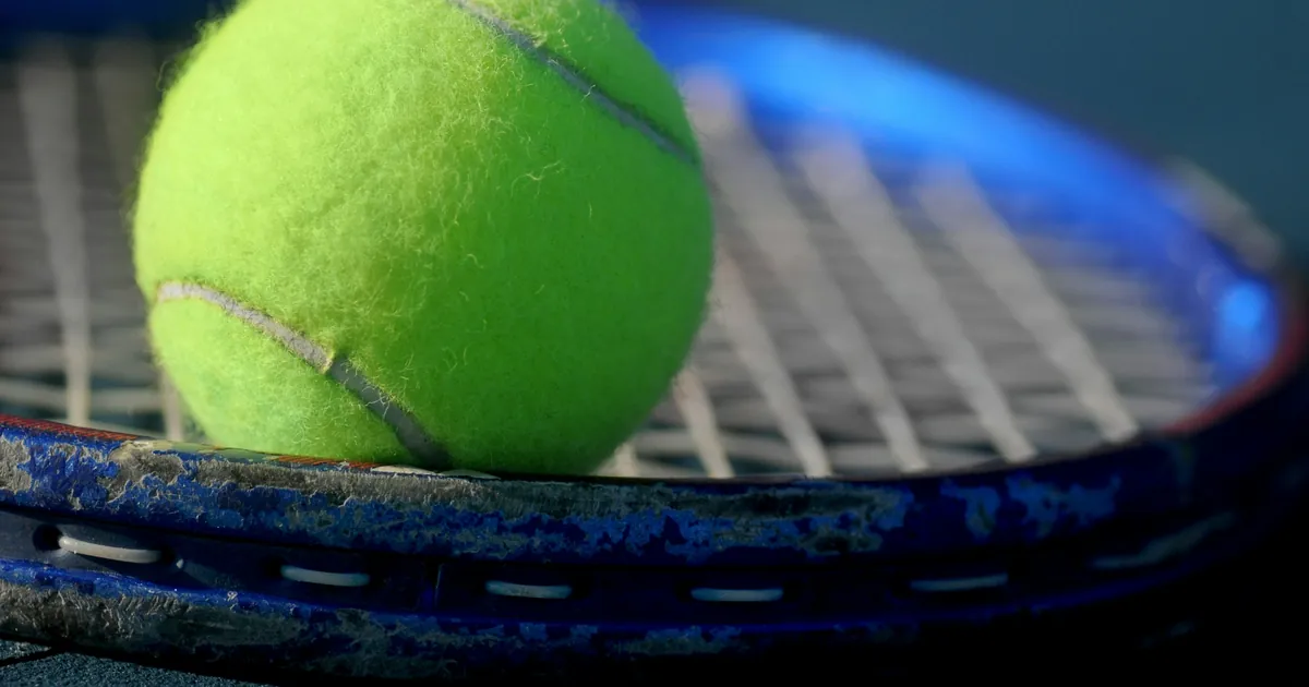 Balle de tennis posée sur le tamis d'une raquette, gros plan sur les cordes