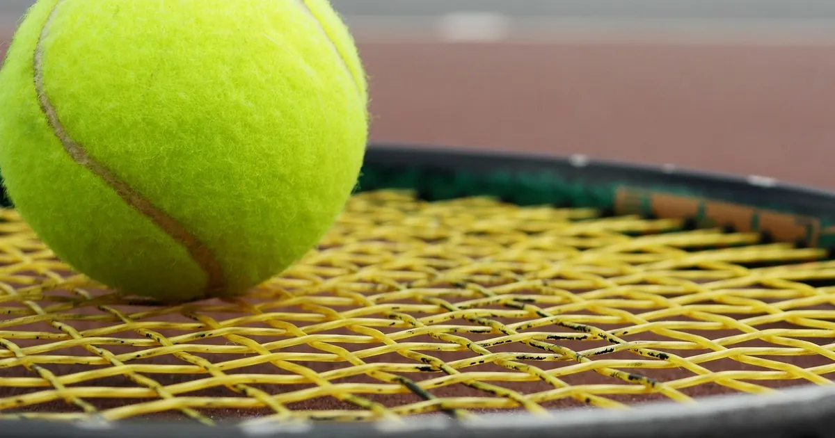 Balle de tennis posée sur un tamis cordé en jaune, au bord d'un court